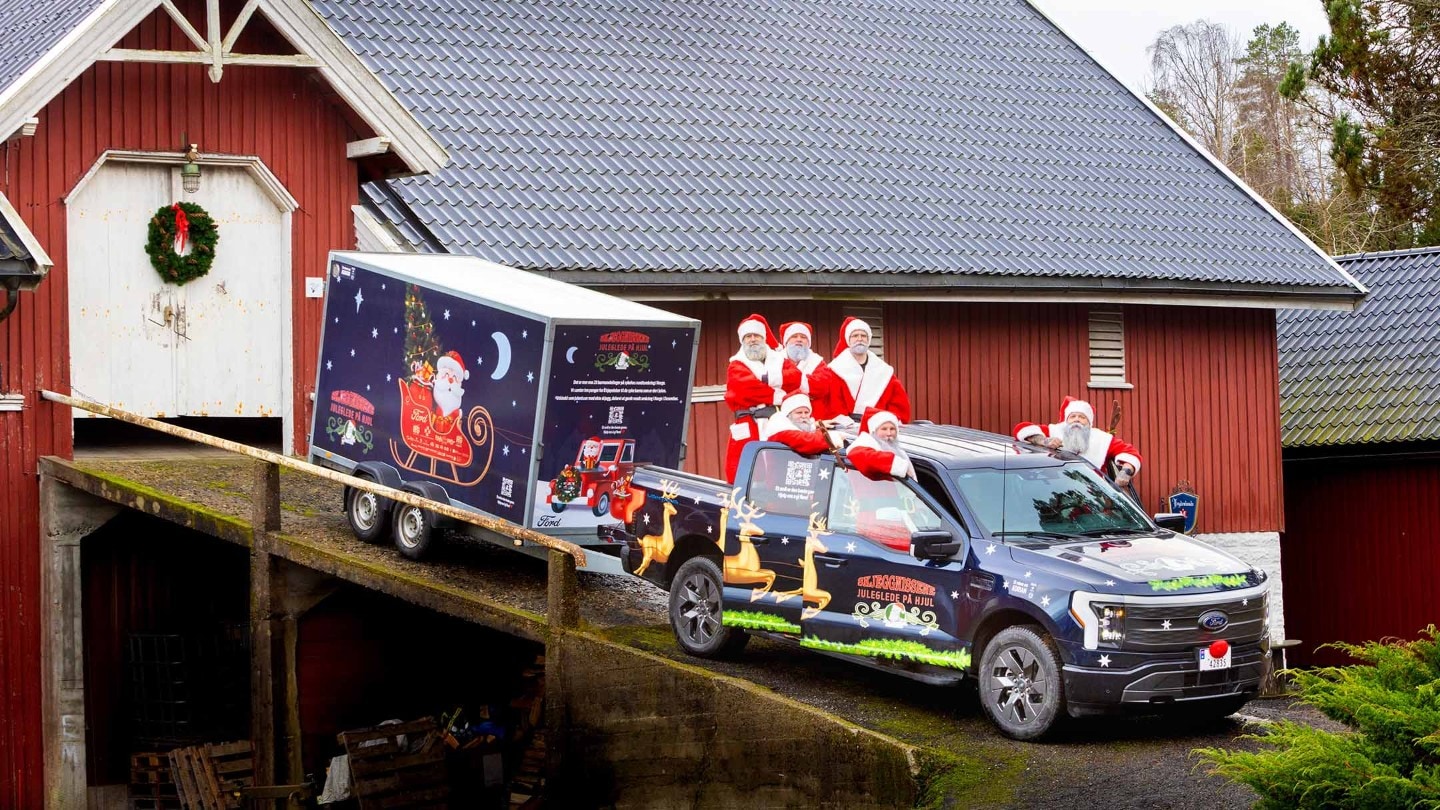 F-150 Lightning parkert ved den portable DNT-turisthytten og tre kvinner sitter utenfor og drikker kaffe.