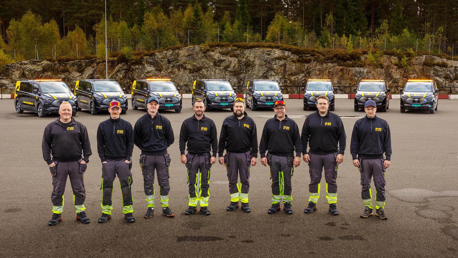 Åtte menn fra Sørby står stilt opp foran en rekke av deres nye Ford varebiler