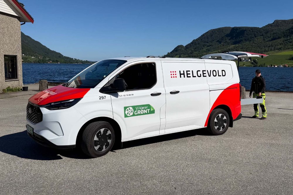 Hvit og rød Ford E-Transit Custom fra Helgevold Elektro parkert ved en fjord
