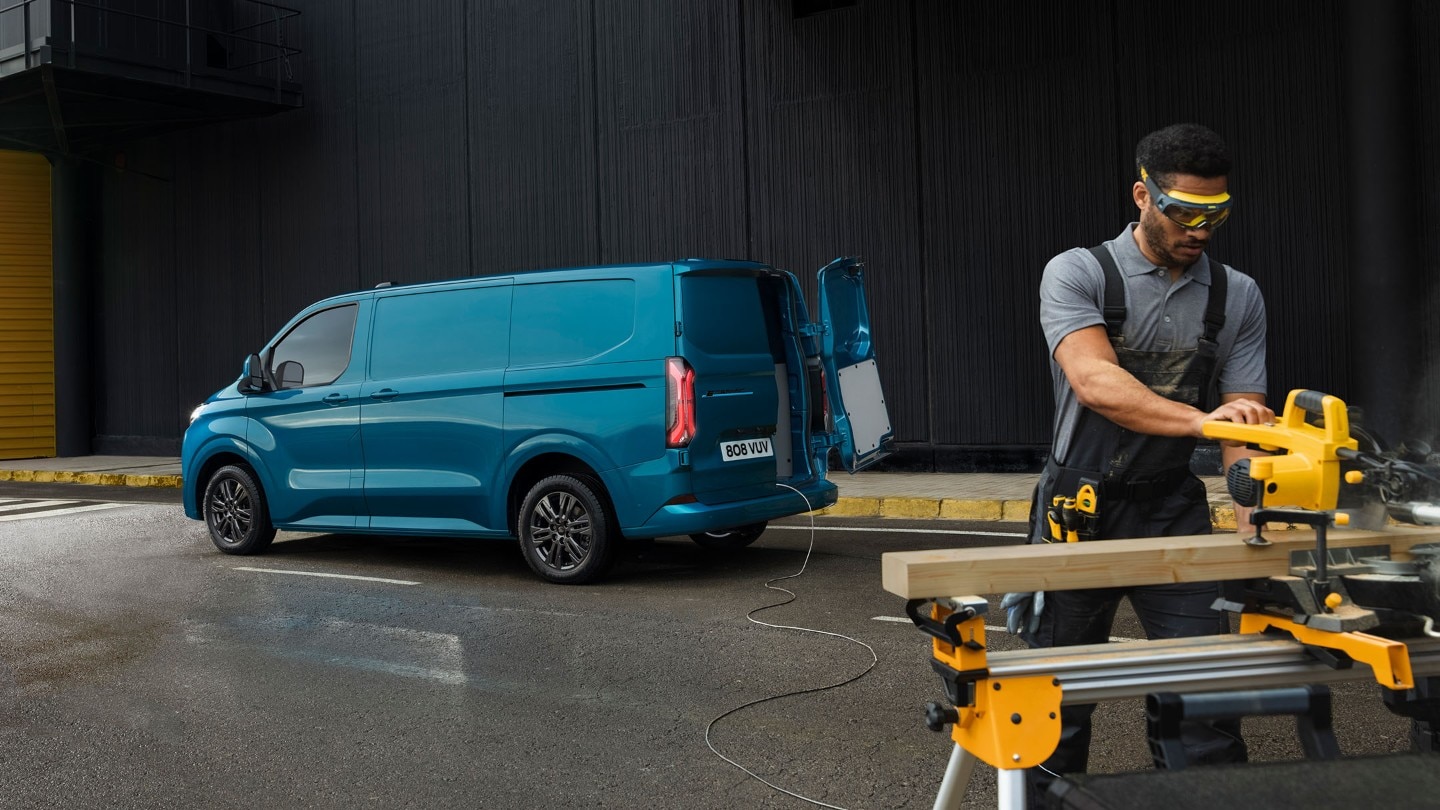En håndverker bruker en sag foran E-Transit Custom