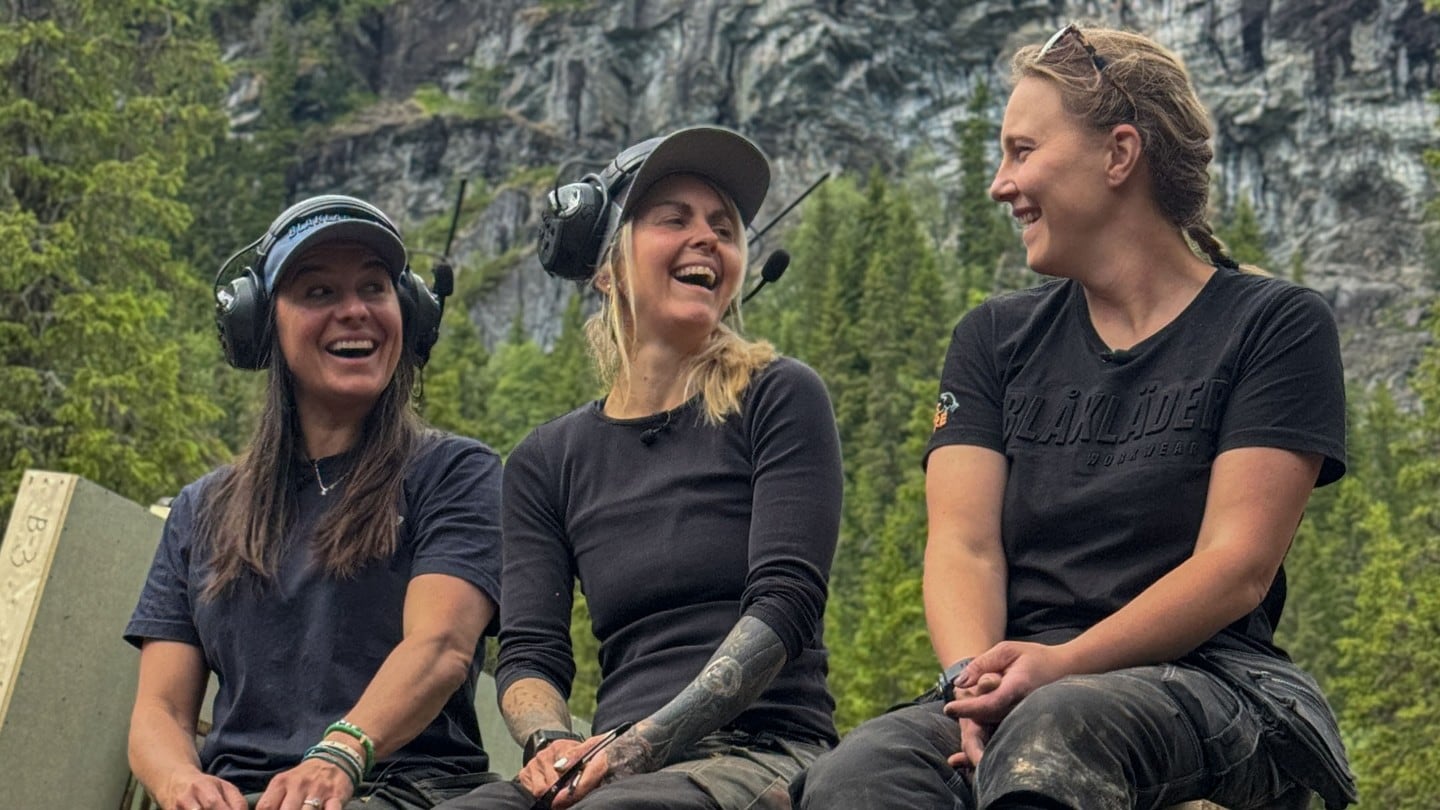 De tre jentene i OssTRE smilende på en trekonstruksjon ute i naturen.  