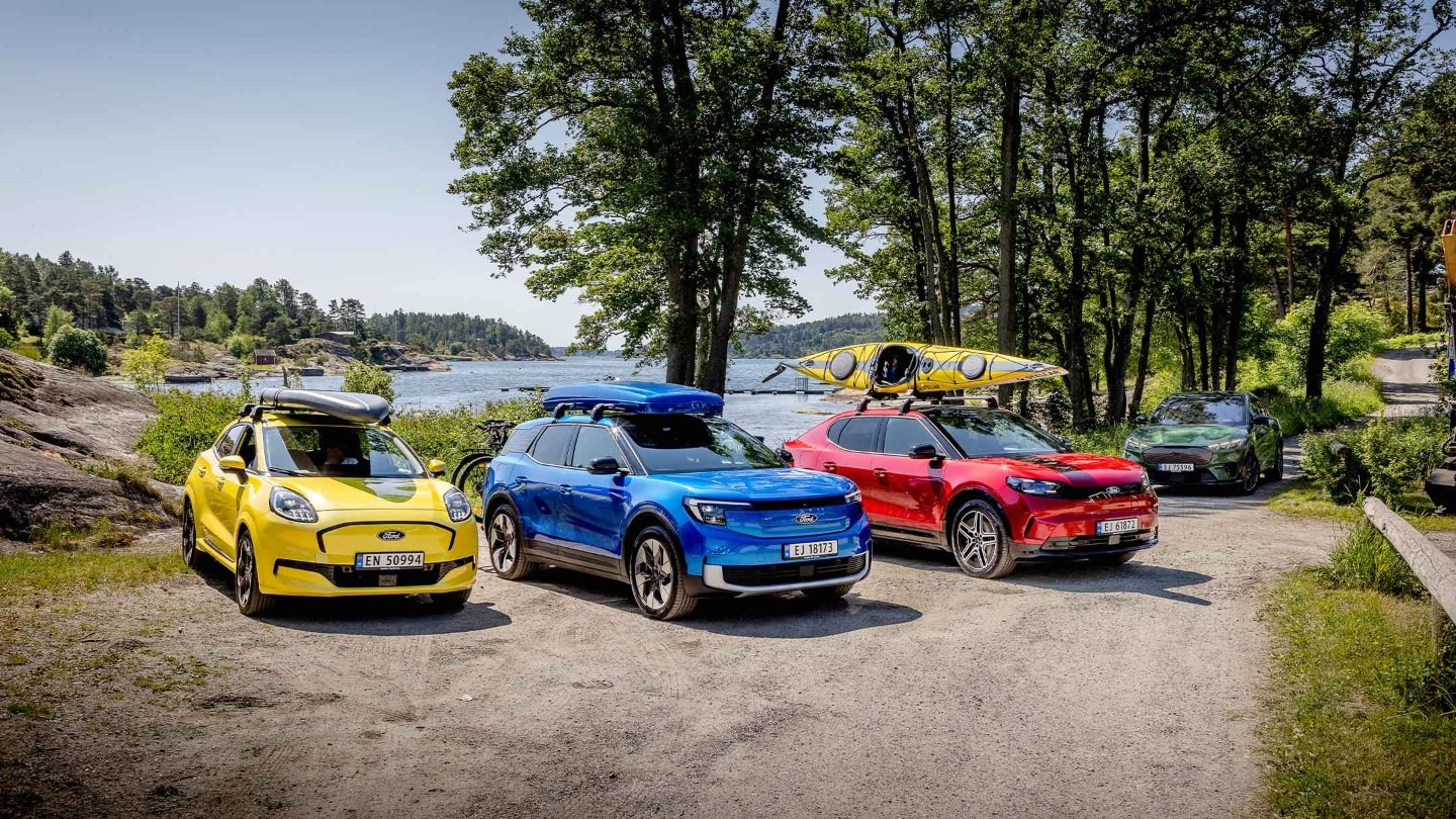 Gul helektrisk Ford Puma med SUP på taket, blå helelektrisk Ford Explorer med takboks på taket og sykler på hengerfestestativ og Rød helelektrisk Ford Capri med kajakk på taket. 