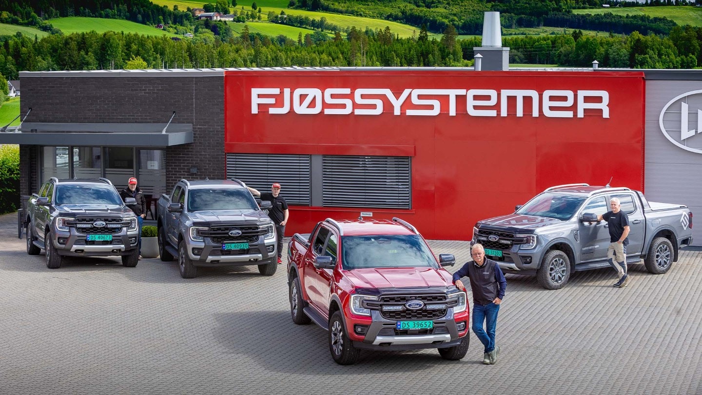Fire Ford Ranger pickuper og fire personer foran en rød bygning med "FJØSSYSTEMER"-skilt.