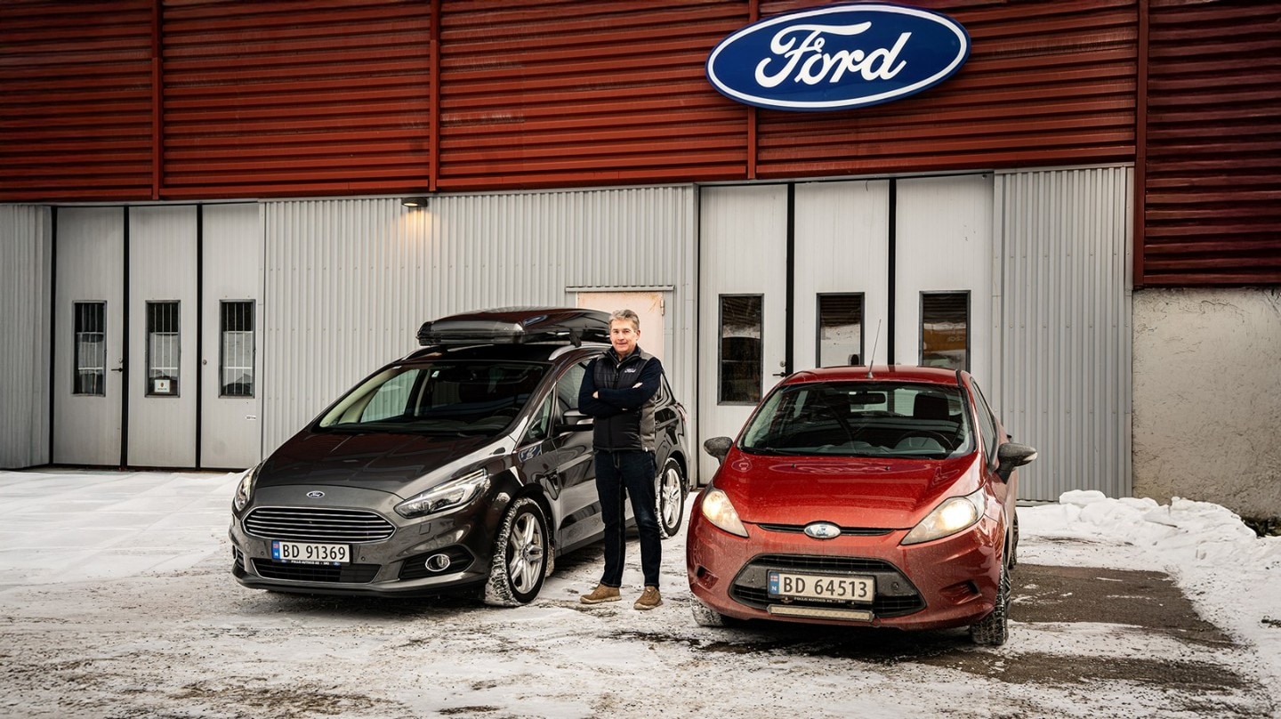 En mann som står utenfor et Ford-verksted mellom en grå Ford S-MAX og en rød Ford Fiesta 