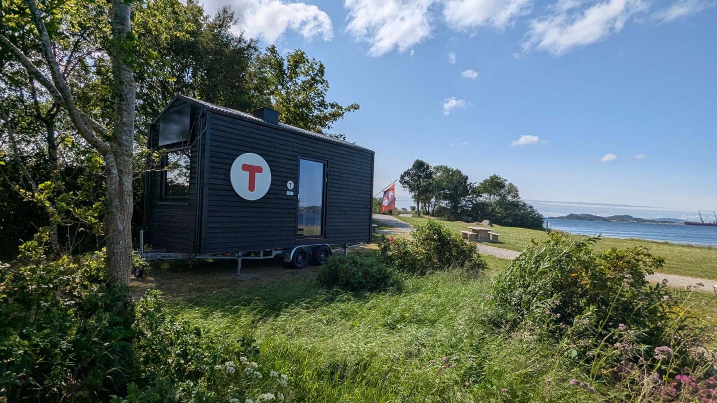Den portable turisthytten står parkert mellom trær nær havet.
