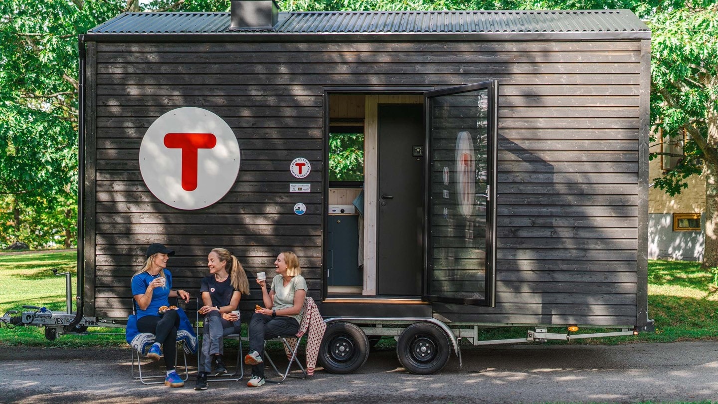 Tre kvinner sitter på stoler foran DNT-hytten og prater sammen.