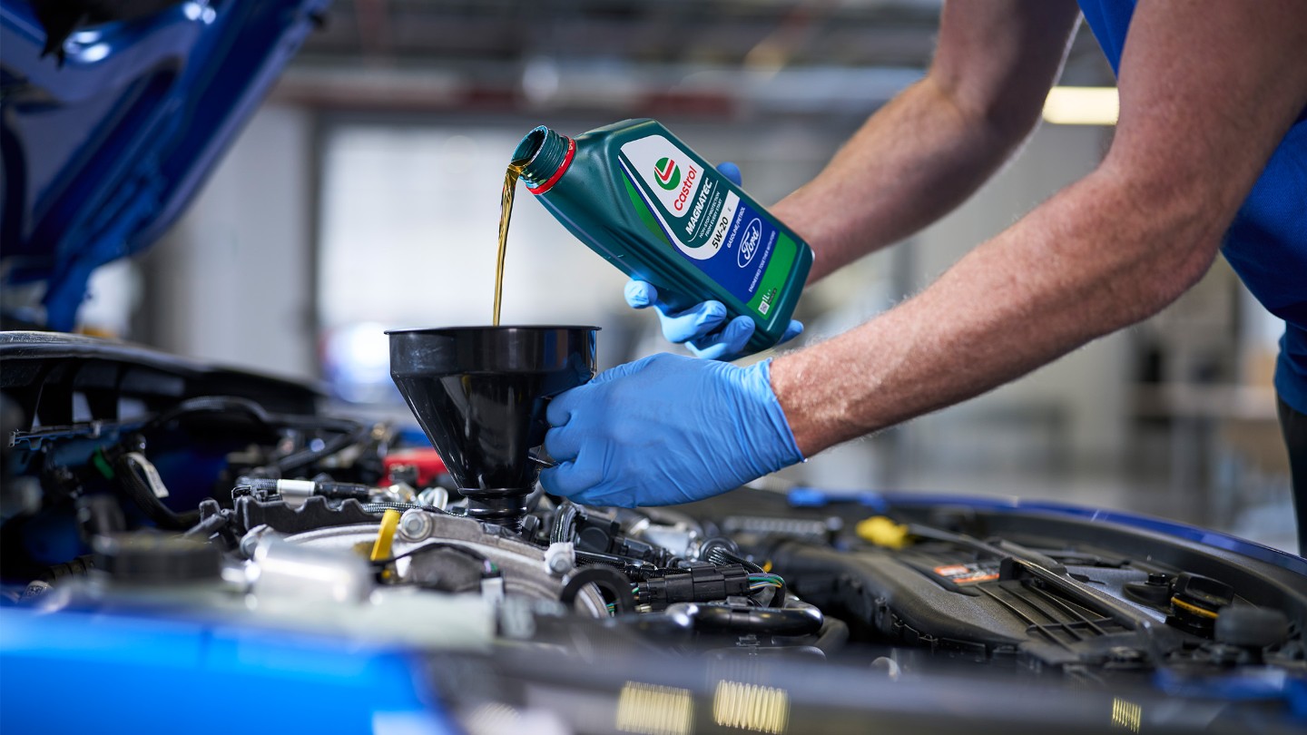 En Ford-tekniker fyller olje på en blå Ford