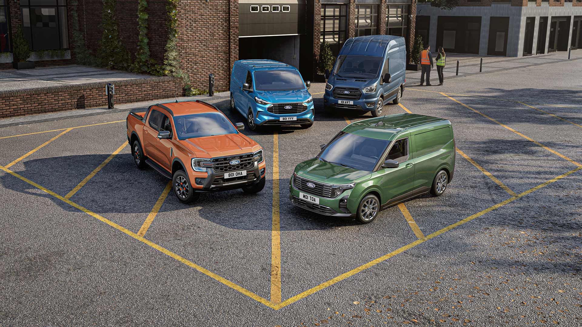 En oransje Ford Ranger og Ford Transit-varebiler parkert utenfor en teglbygning, med to personer i nærheten.