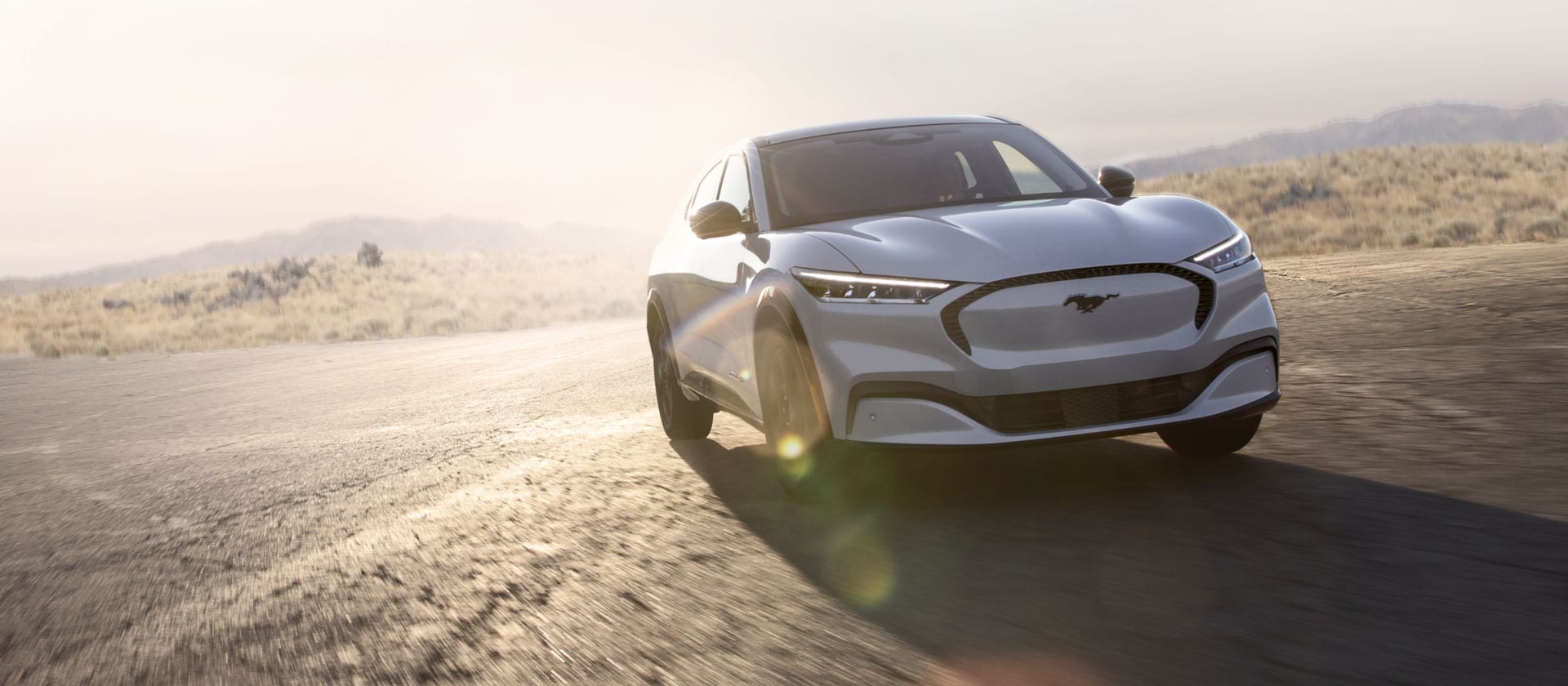  En sølvfarget Ford Mustang Mach-E som kjører på en lang, åpen vei.