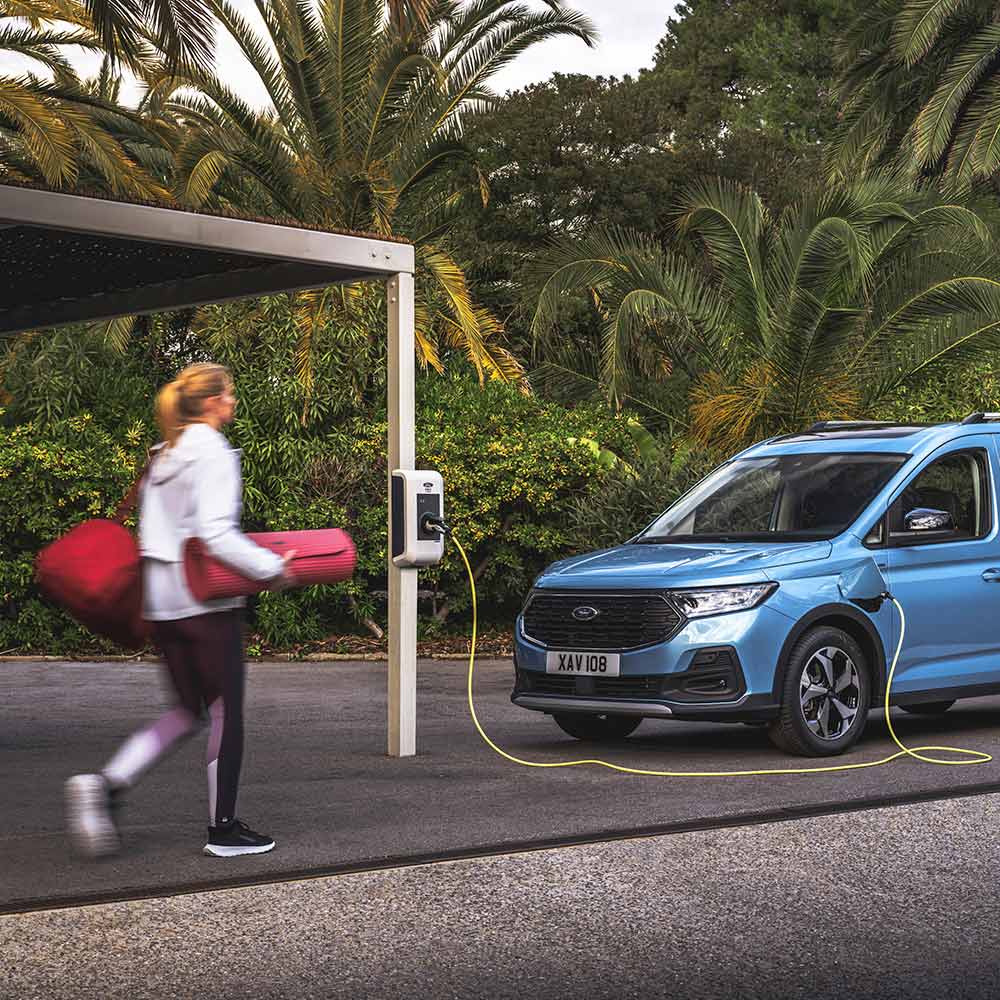 En person går med en yogamatte mot en Ford Tourneo Connect plug-in hybrid varebil.