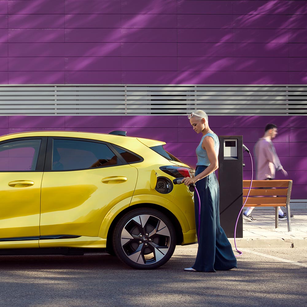 En fører plugger en sølvfarget Ford Puma Gen-E inn i en offentlig ladestasjon for enkel lading.