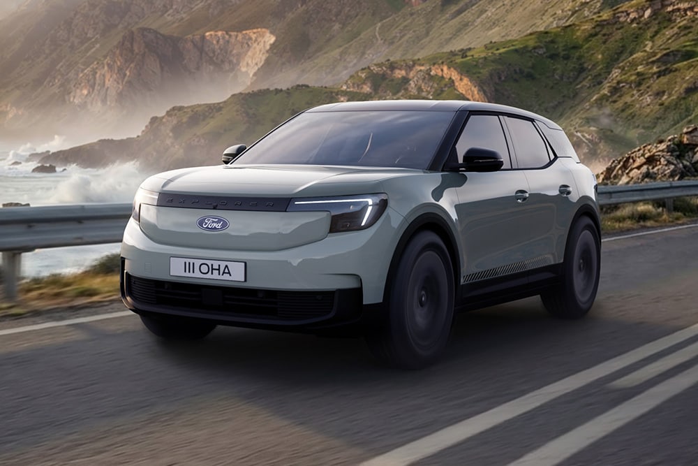 A grey Ford Explorer driving along a coastal road with mountains and the sea in the background. 