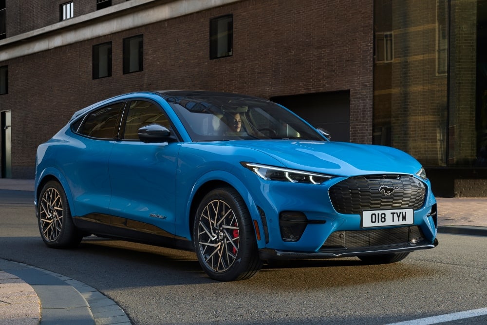 A blue Ford Mustang Mach-E electric SUV parked on an urban street.