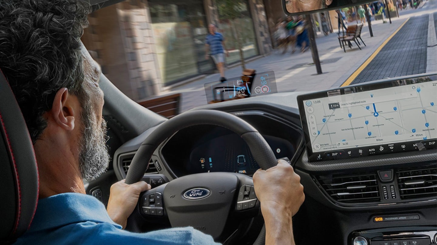 Interiørbilde av en mann som kjører Ford Kuga langs en byvei. 