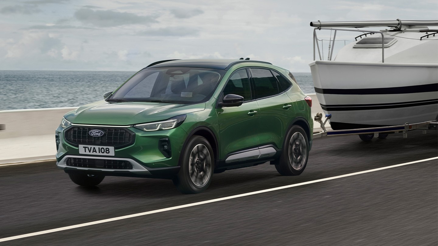 En grønn Ford Kuga som sleper en liten båt langs en kystvei.