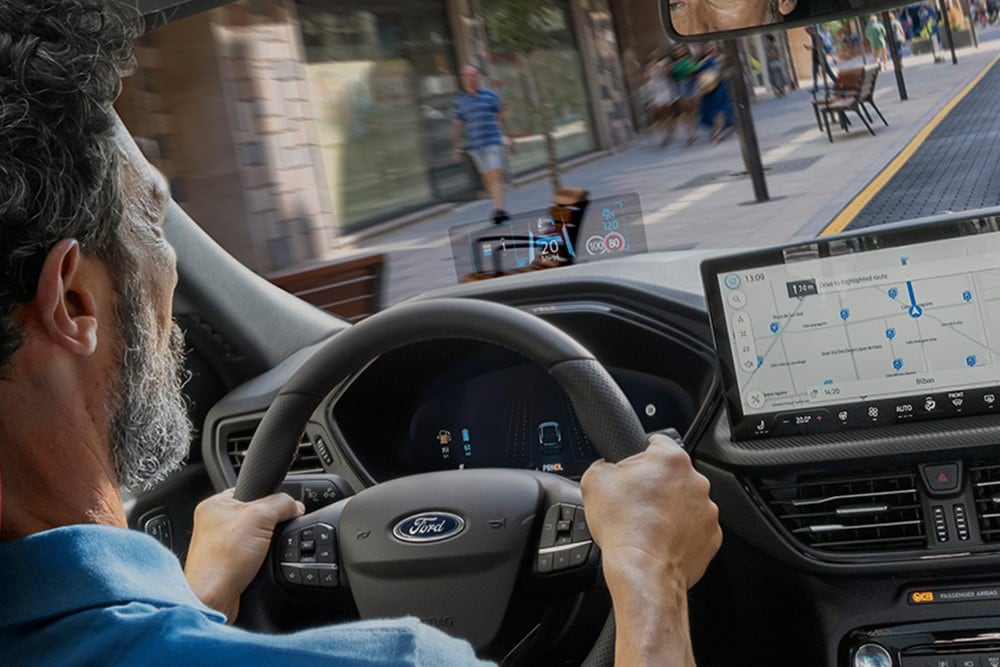 Interiørbilde av en mann som kjører Ford Kuga langs en byvei. 