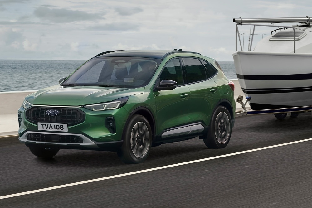 En grønn Ford Kuga som sleper en liten båt langs en kystvei.