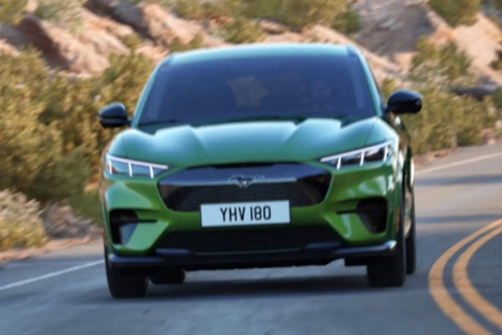 Grønn Ford Mustang Mach-E sett forfra kjørende på en svingete vei.