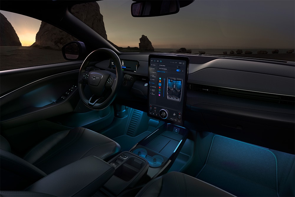 Interiøret i Ford Mustang Mach-E om natten, med visning av den 15,5-tommers SYNC 4-touchskjermen og LED-stemningslys stilt til blå.
