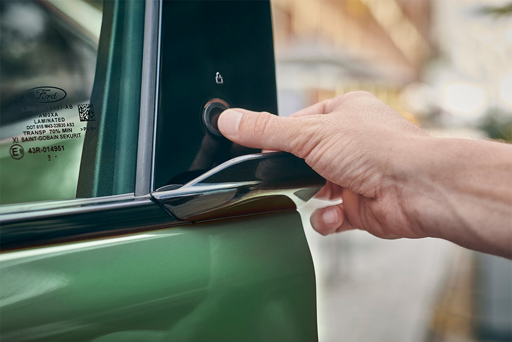 Et nærbilde av en hånd som betjener E-Latch-systemet ved å trykke på en knapp på døren til en grønn Ford Mustang Mach-E.