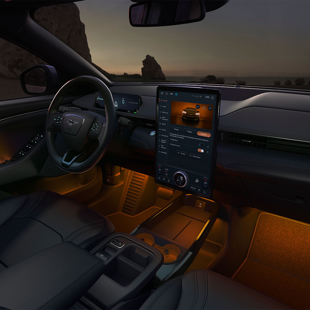 The interior of the Ford Mustang Mach-E at night, showing the 15.5" SYNC 4 touchscreen and ambient LED lighting set to orange