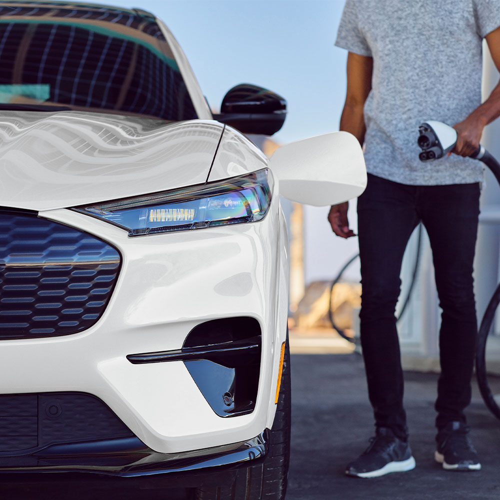 En person som lader en hvit Ford Mustang Mach-E med ladekabel.