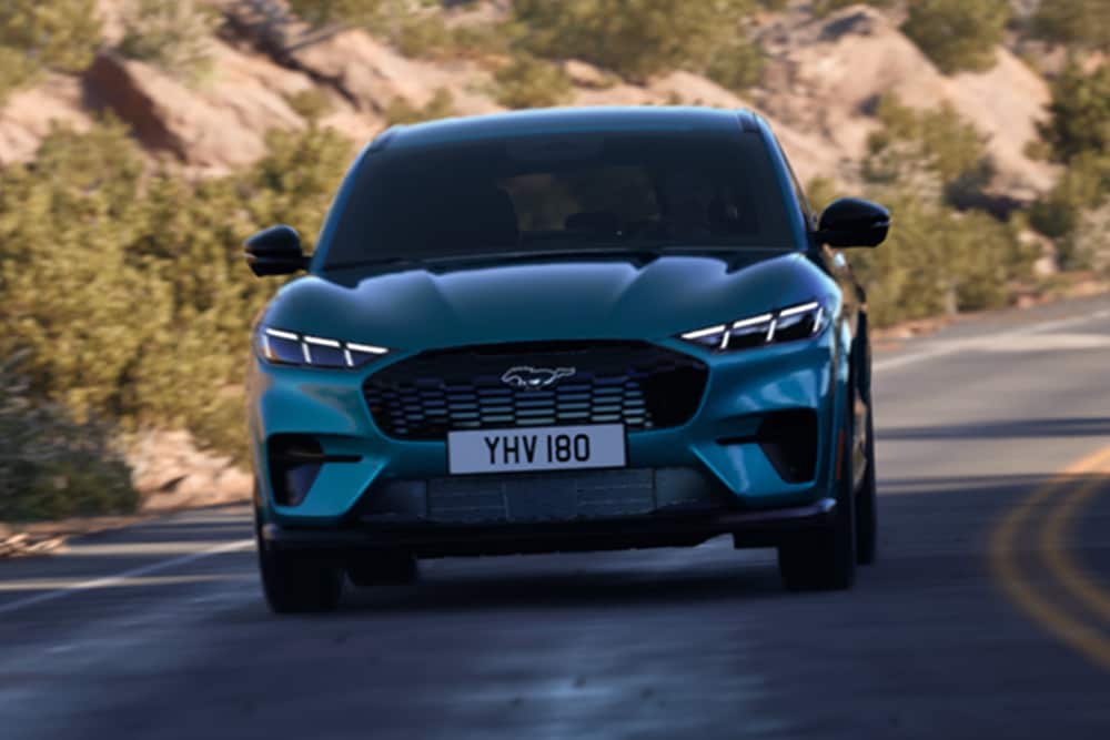 Frontvisning av en blå Ford Mustang Mach-E som kjører på en fjellvei.