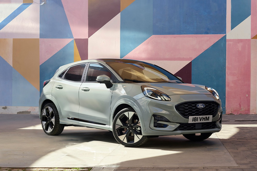 En sølvfarget Ford Puma SUV parkert foran et fargerikt geometrisk veggmaleri.