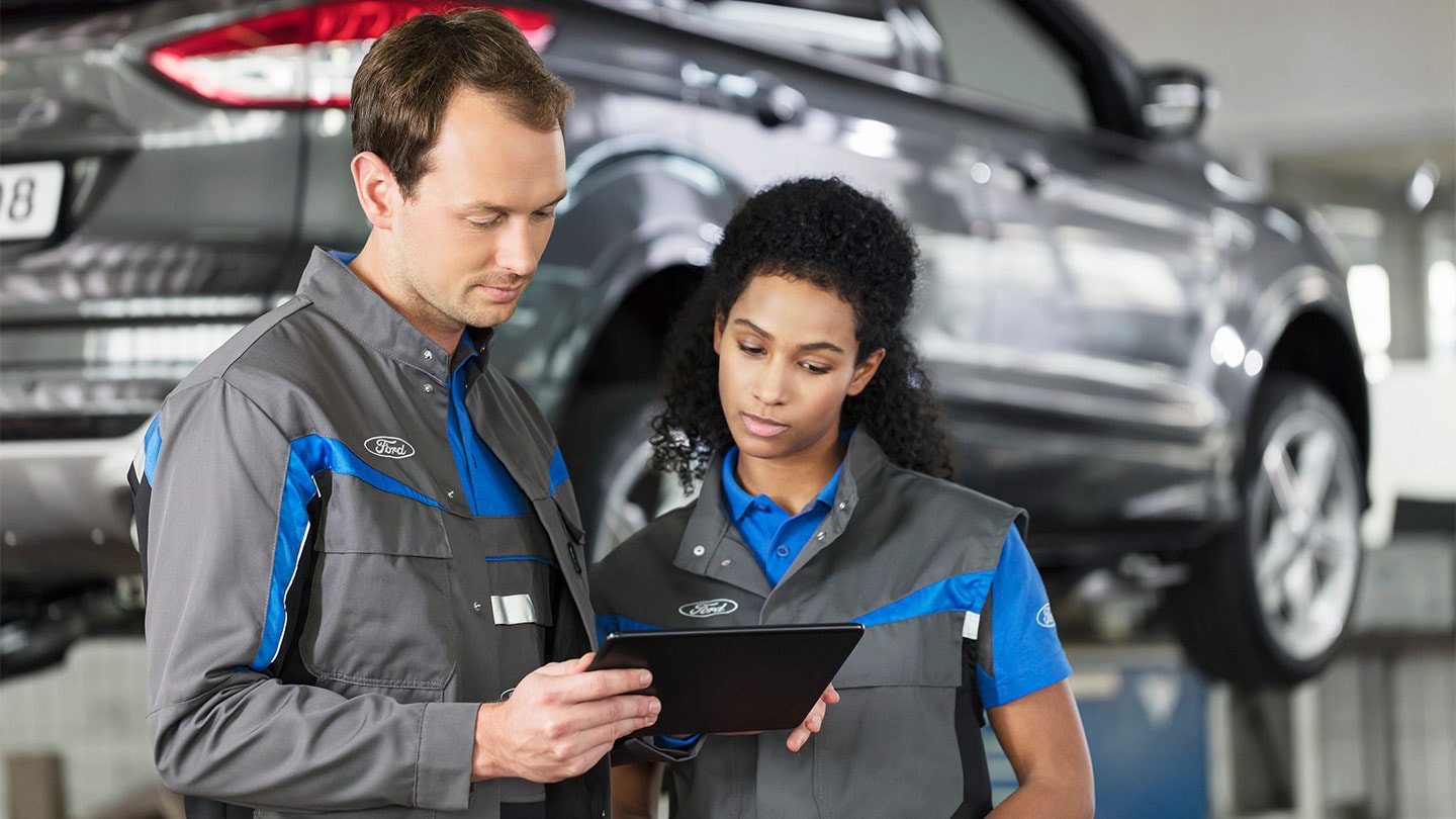 To Ford-reparasjonspesialister sjekker sitt online servicebookingsystem på en telefon.