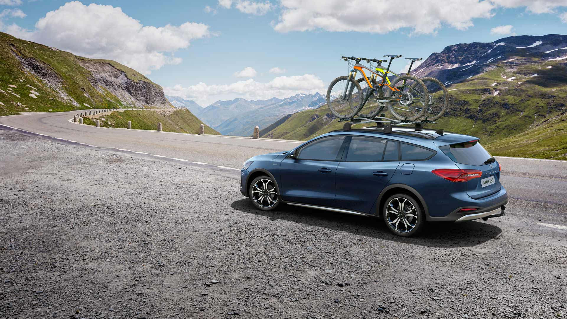 Blå Ford Focus med sykler på taket som kjører langs en naturskjønn fjellvei.