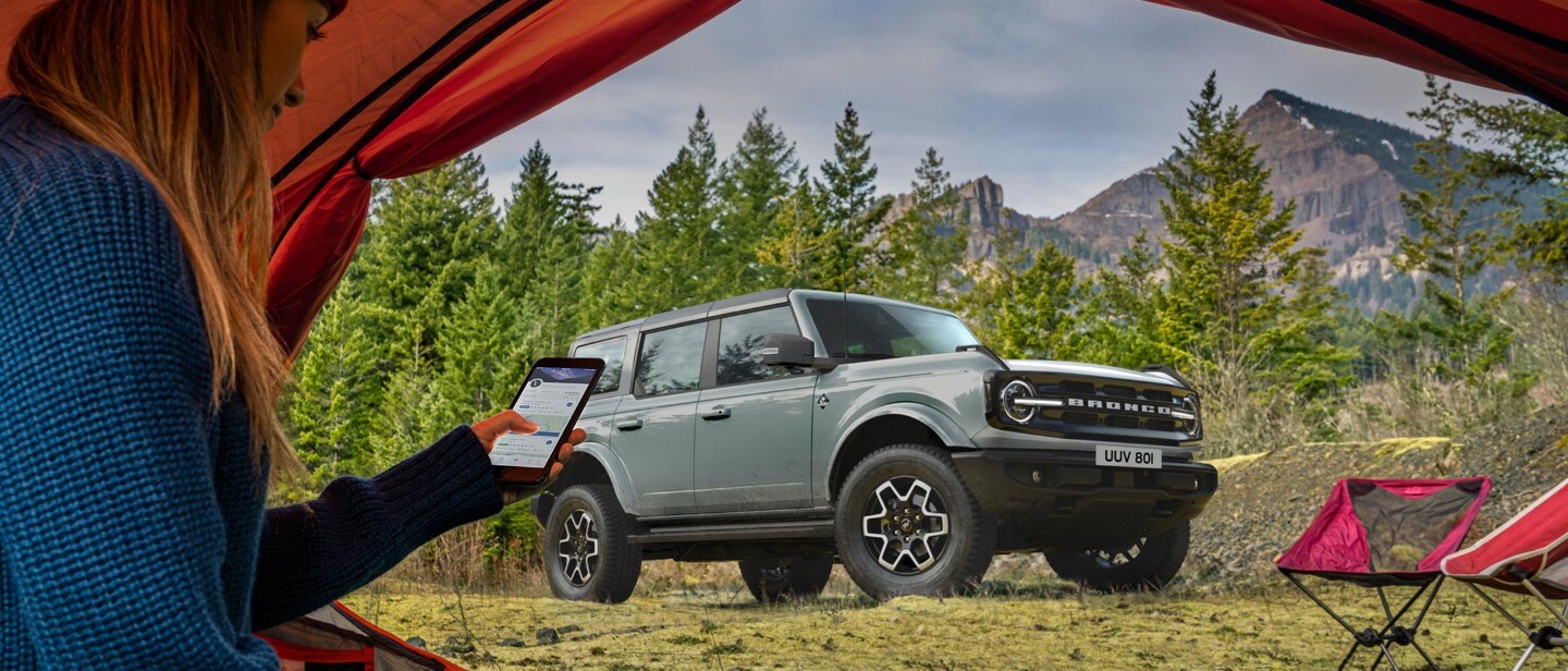 Person looking at the FordPass app on her smartphone with Ford Bronco parked in the background