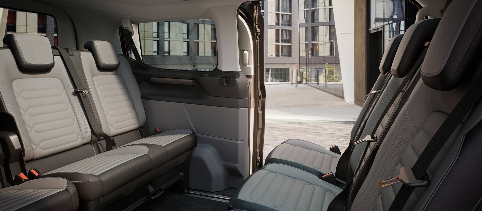 Interiørvisning av Ford Tourneo Custom, som viser flere rader med grå passasjerseter og soltak med panoramautsikt.