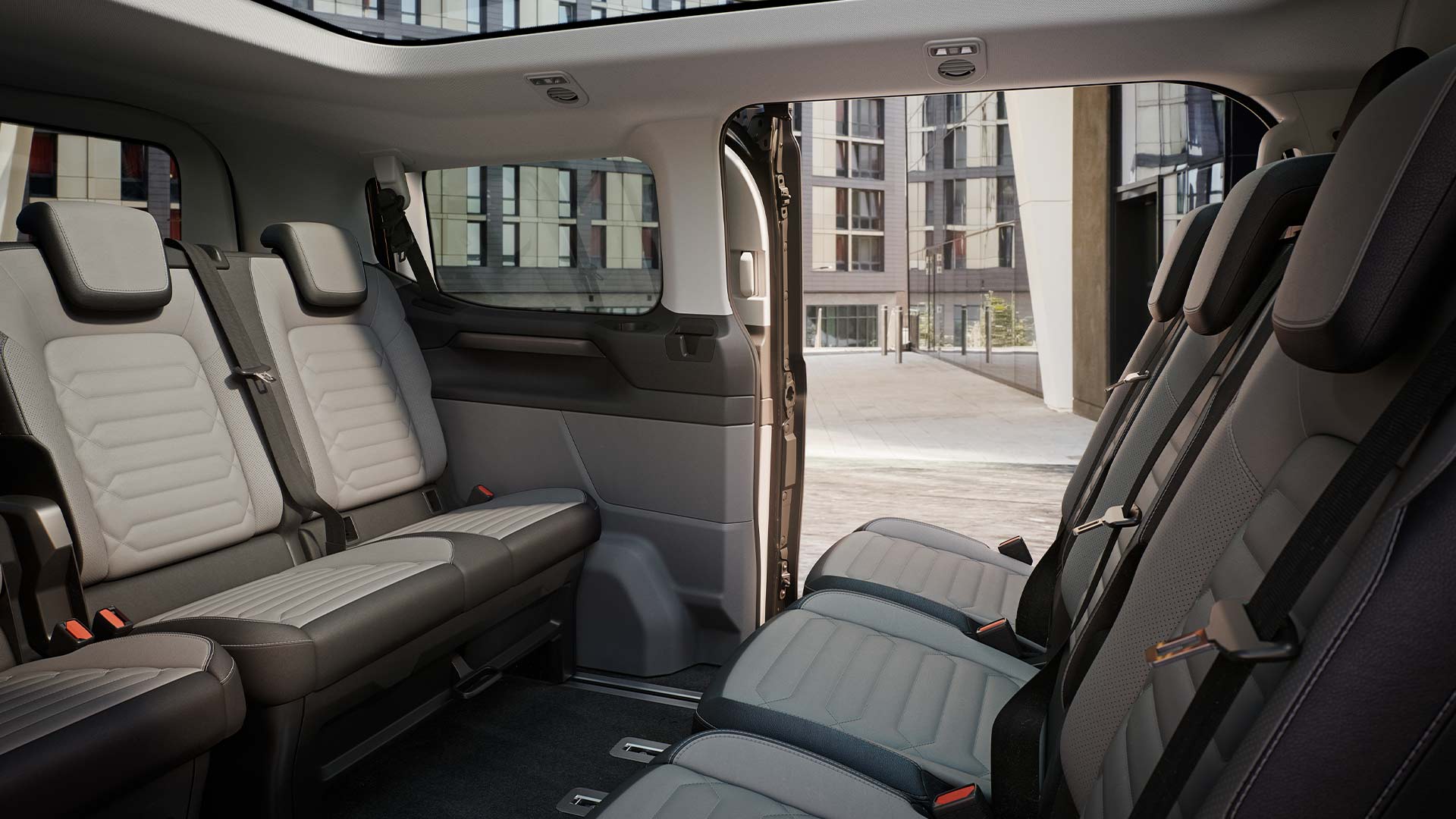 Interiørvisning av Ford Tourneo Custom, som viser flere rader med grå passasjerseter og soltak med panoramautsikt.