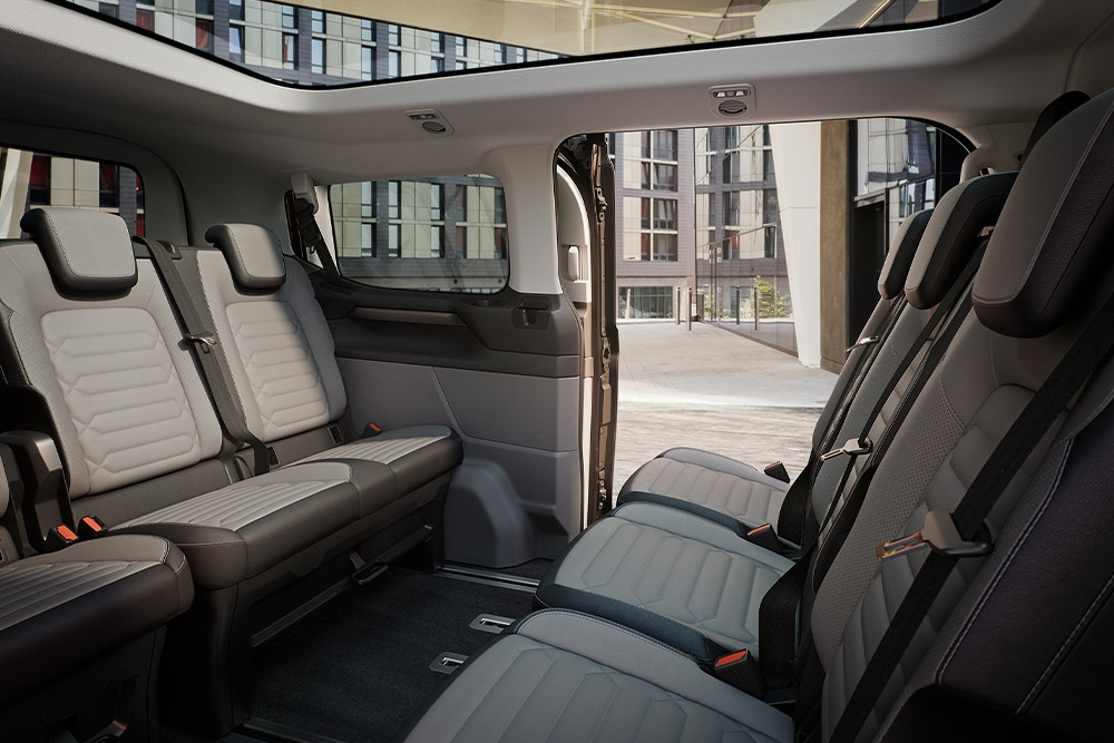 Interiørvisning av Ford Tourneo Custom, som viser flere rader med grå passasjerseter og soltak med panoramautsikt.