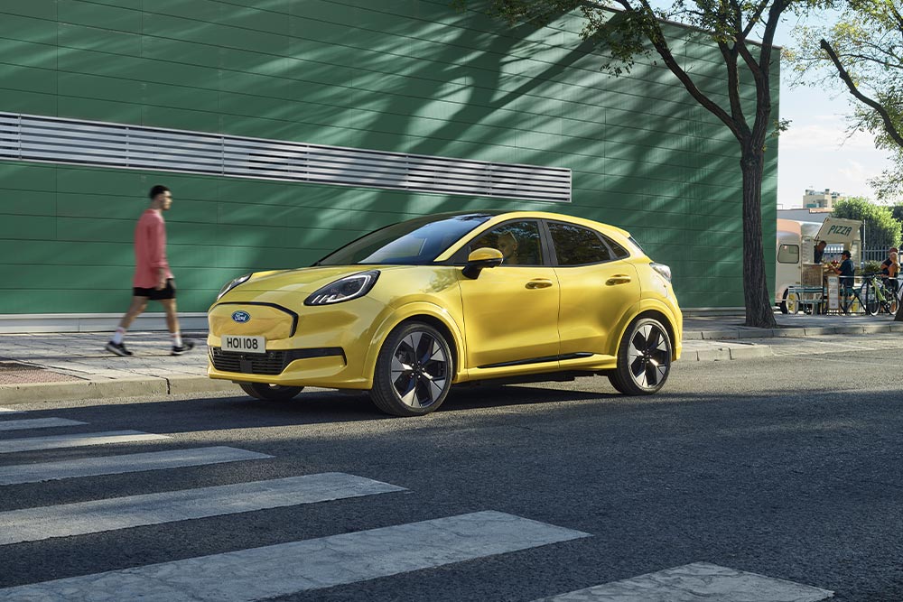 Sidevisning av en gul elektrisk Ford Puma®, parkert i en veikant.