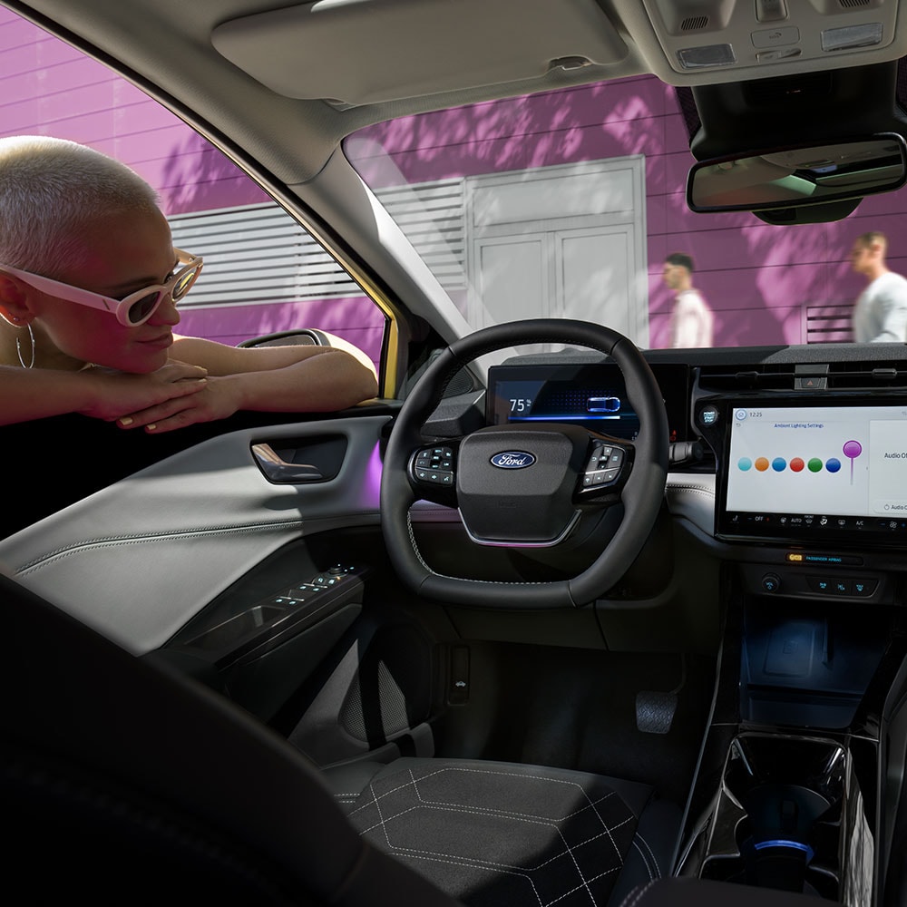 Interiøret i elektriske Ford Puma®, med en person som ser på den store infotainmentskjermen gjennom vinduet.