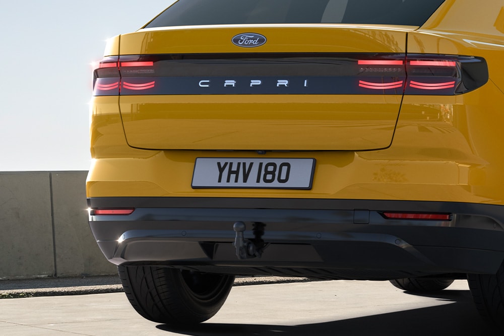 Visning bakfra av en gul Ford Capri® som kjører på en urban vei.