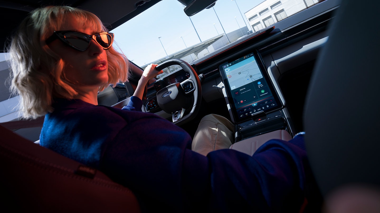 En kvinne sitter i førersetet på en parkert Ford Capri®, med rattet og den store SYNC® Move-touchskjermen synlig.