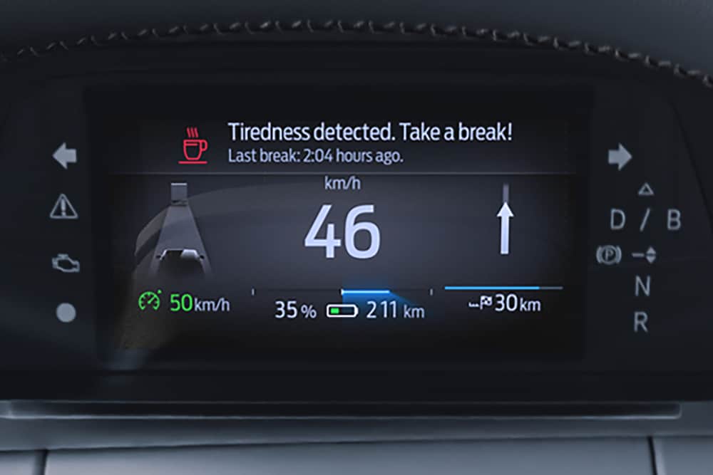 Det digitale kombiinstrumentet i Ford Capri, som viser bilens hastighet og et førervarsel med en advarsel som anbefaler å ta en pause.