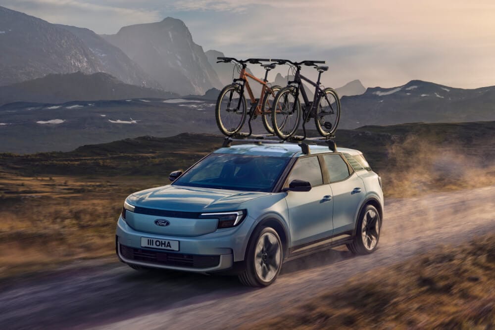 Blå Ford Explorer kjører på støvete vei, med tverrstenger, sykkelstativ og to sykler på taket.