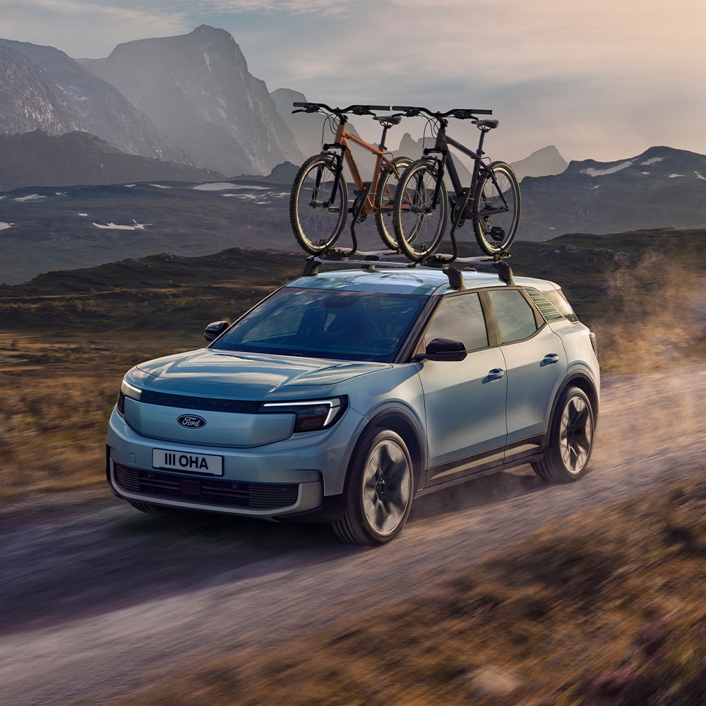 Blå Ford Explorer kjører på støvete vei, med tverrstenger, sykkelstativ og to sykler på taket.