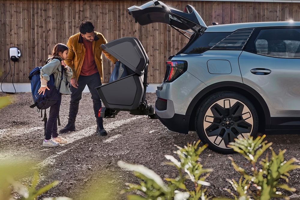 En mann med barn står ved siden av det åpne bagasjerommet på en Ford Explorer SUV,, og laster inn en sammenleggbar barnevogn.