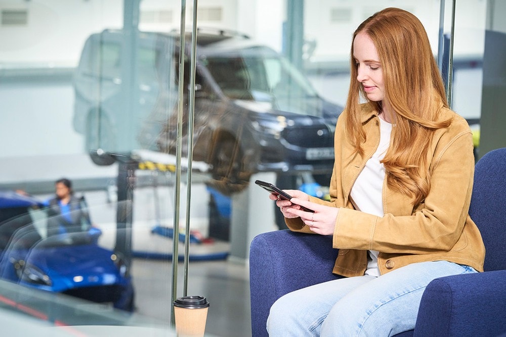 En person som sitter på en kontorpult med en laptop og en smarttelefon, i et moderne kontorlandskap.