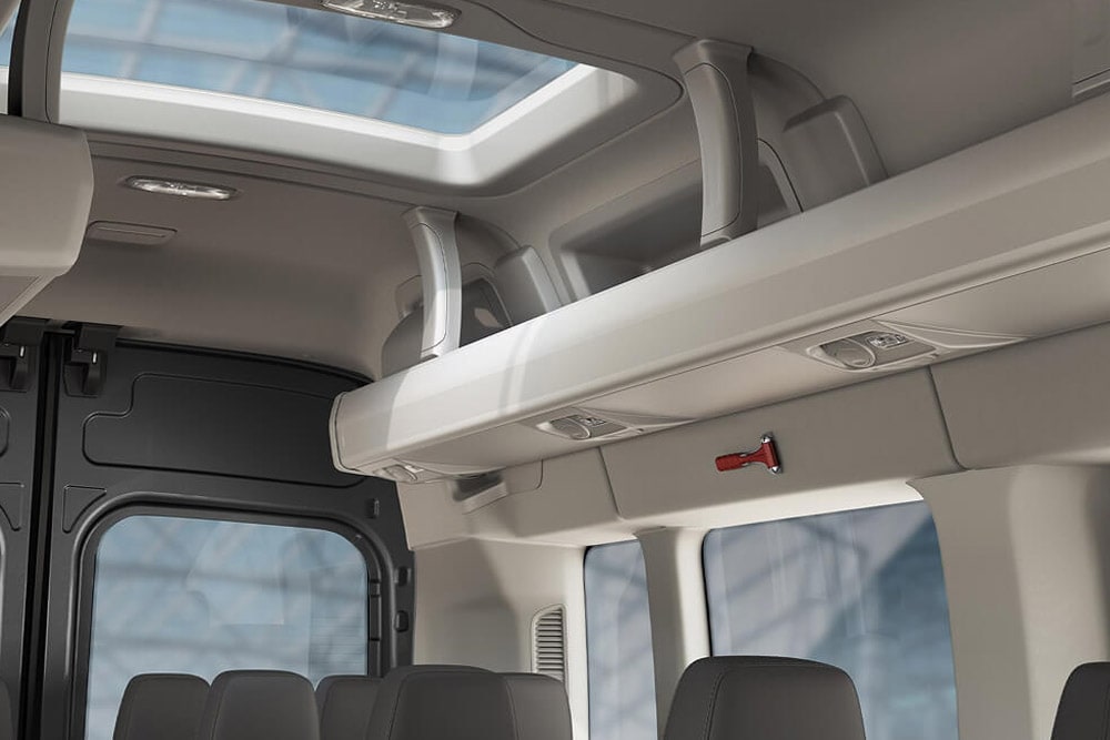 Interiøret i en Ford Transit Minibuss som viser et soltak, oppbevaring i taket og en nødhammer over passasjersetene.