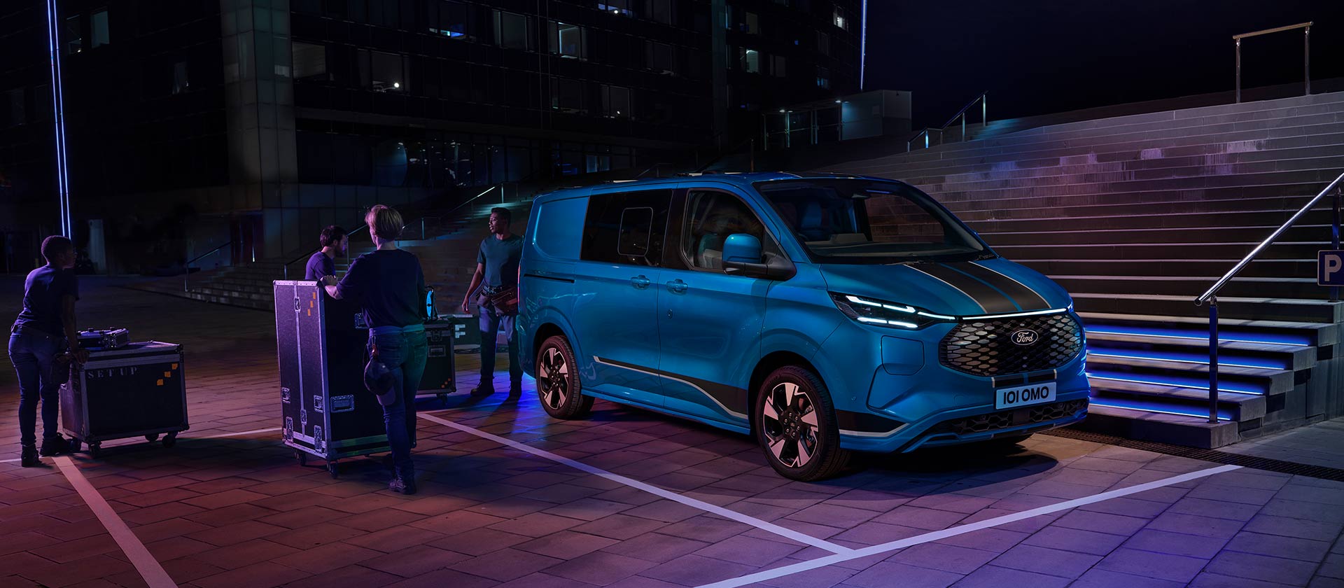 Blå elektrisk Ford E-Transit Custom-varebil som lastes om natten.