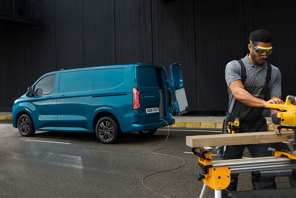 Blå elektrisk Ford E-Transit Custom-varebil og en person som bruker elektroverktøy.