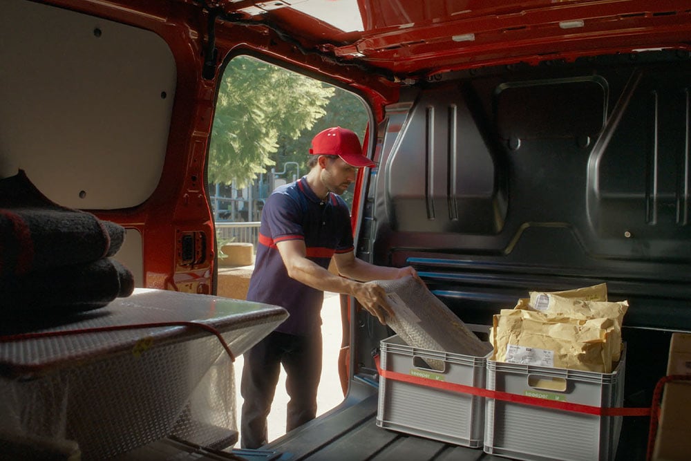 Budsjåfør laster pakker inn i en rød Ford E-Transit Custom.