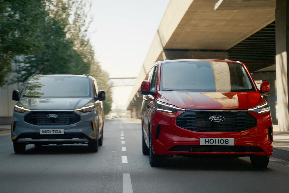 En grå og rød Ford Transit Custom-varebil kjører langs en motorvei.