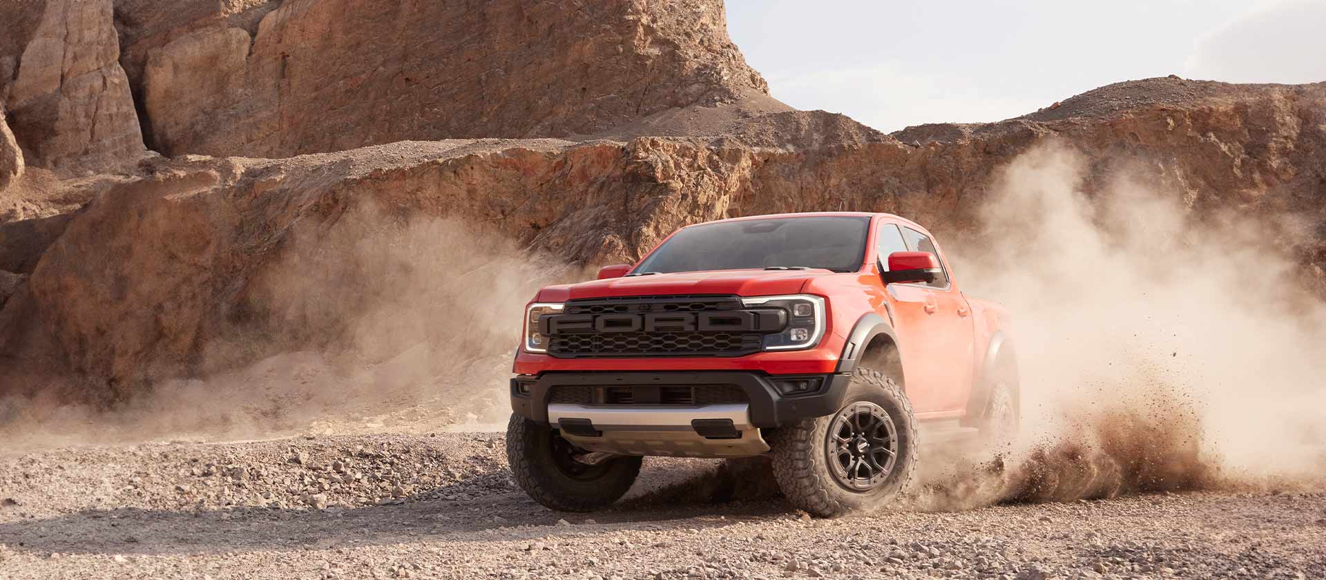  Ford Ranger Raptor i fargen Code orange kjører gjennom støv og småstein.