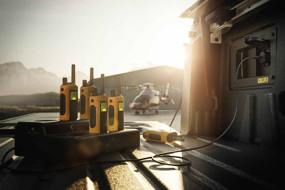 Walkietalkier som lades på lasteplanet i en Ranger Raptor ved solnedgang, med et helikopter i bakgrunnen.